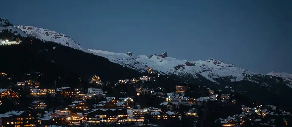 Snowy ridge at dusk above a village with lit windows